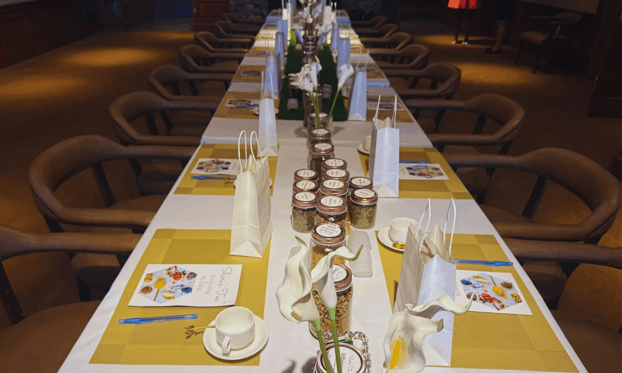 Elegant long-table tea-tasting and blending setup with custom tins and gold place settings